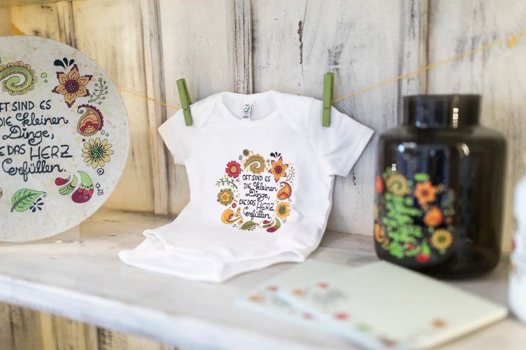 Bild von einem bedruckten Glasteller, einem Babybody mit dem Motiv "die kleinen Dinge" und einer Vase