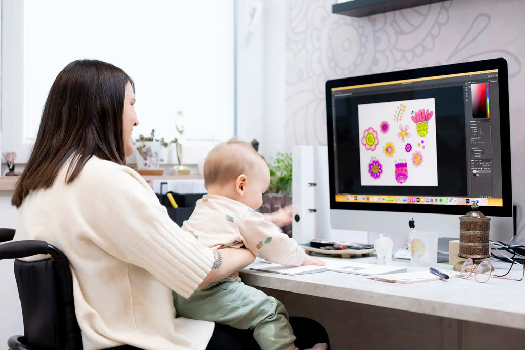 Tina sitzt mit Baby am Arm vor dem PC. Beide lachen