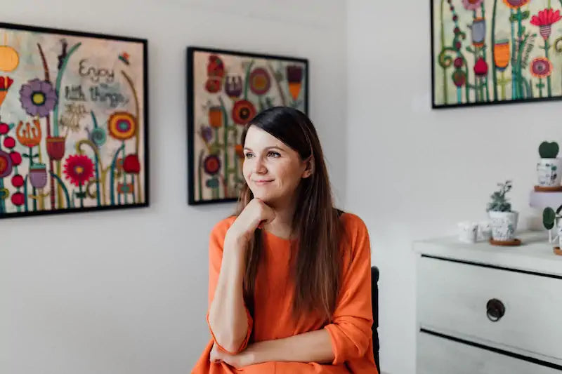 Tina sitzt in ihrer Galerie vor einigen ihrer einzigartigen Bildern die sie gemalt hat