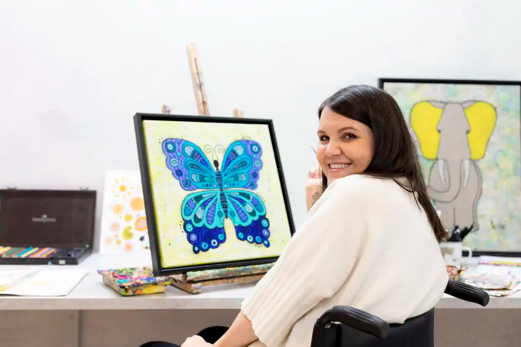 Tina zeichnet einen Schmetterling und lächelt dabei. Im Hintergrund ist ein Bild eines Elefanten